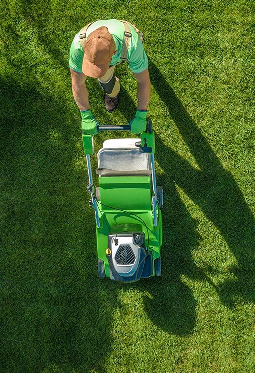 An aerial view of a man pushing a green lawn mower on a lush green lawn.