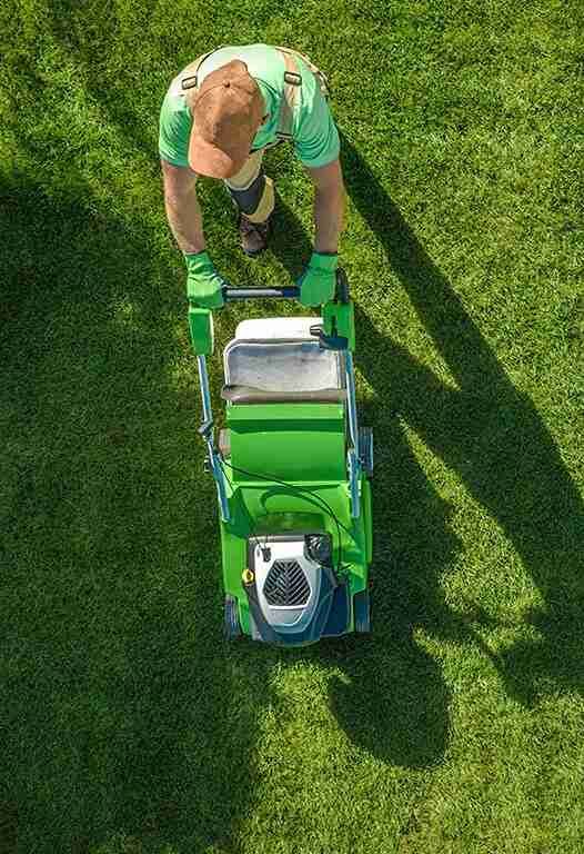 An aerial view of a man pushing a green lawn mower on a lush green lawn.