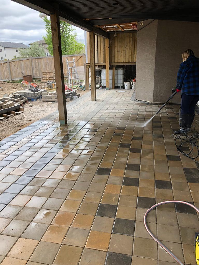 A man is cleaning a patio with a high pressure washer.