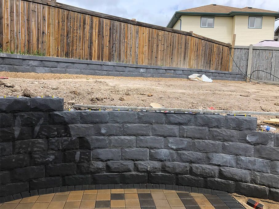 A brick wall is being built in a backyard with a wooden fence in the background.