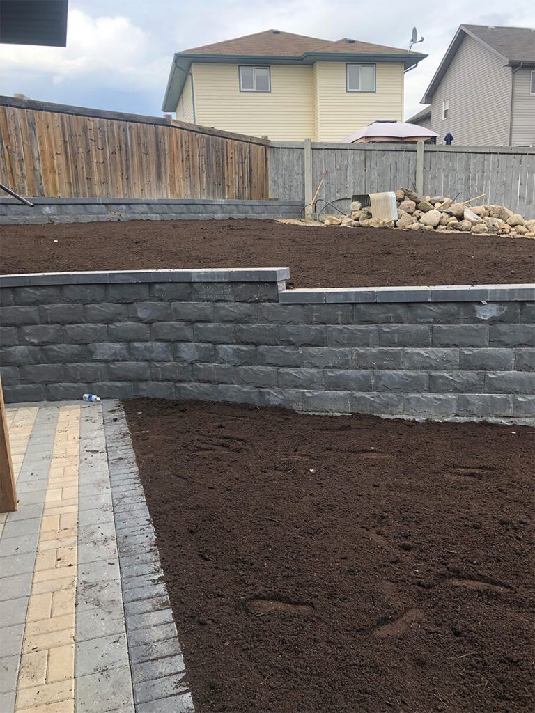 A backyard with a brick wall and a pile of dirt