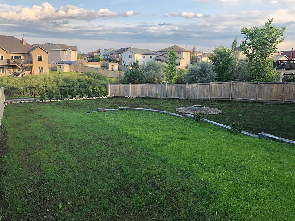 A large lush green yard with a wooden fence and houses in the background.