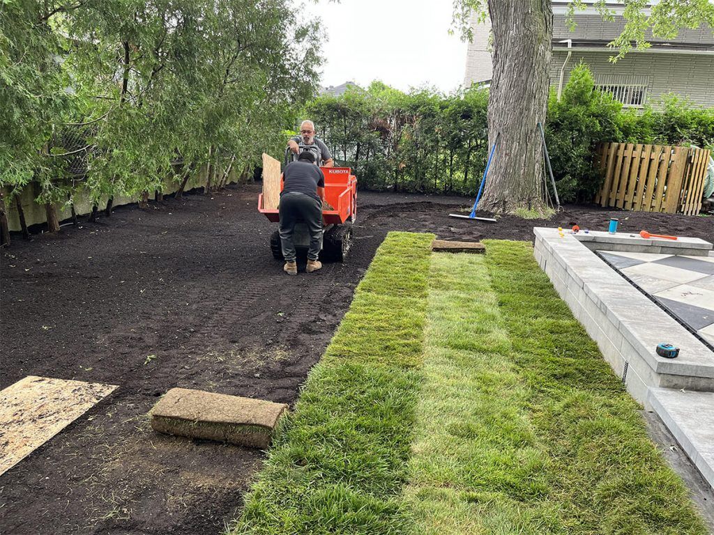 A man is driving a tractor through a lush green yard.