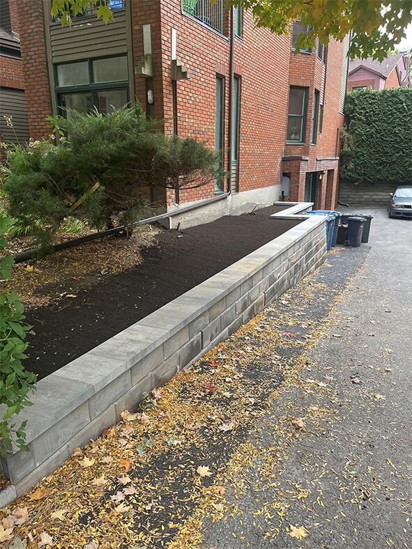A brick wall surrounds a lush green garden in front of a brick building.