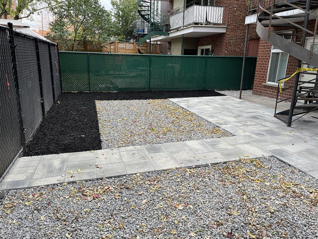 A gravel yard with a chain link fence and stairs in front of a building.
