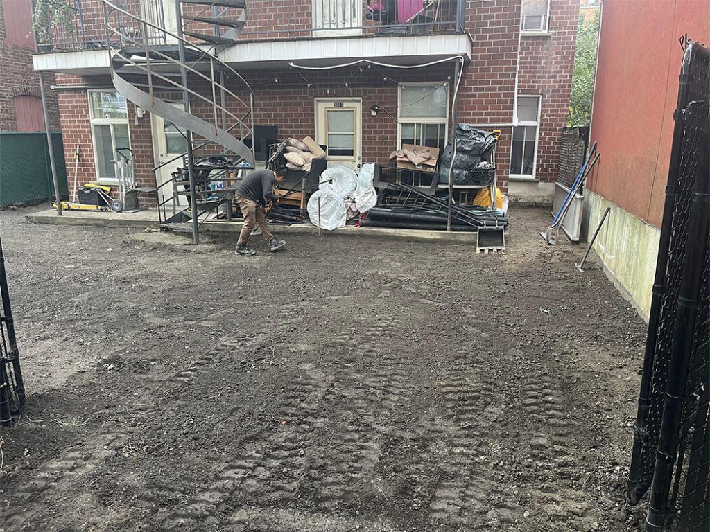 A man is digging in the dirt in front of a brick building.