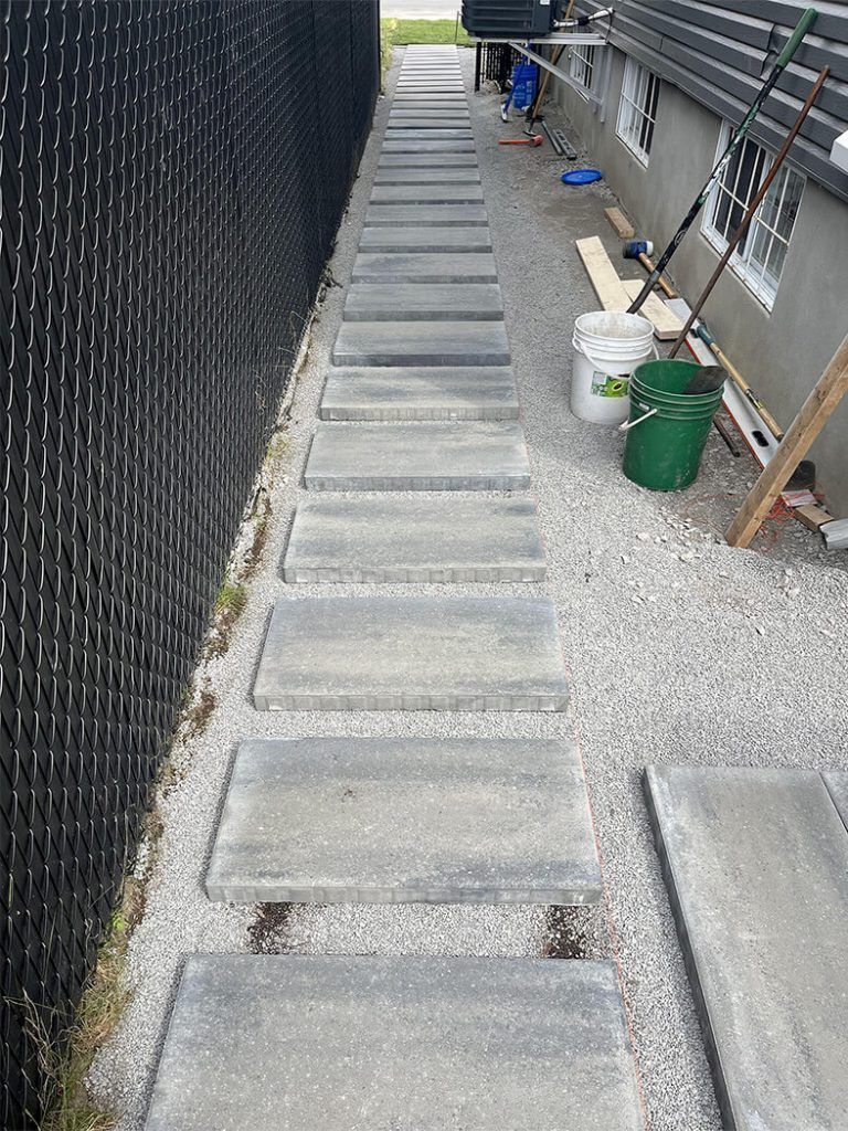 A concrete walkway leading to a house next to a chain link fence.