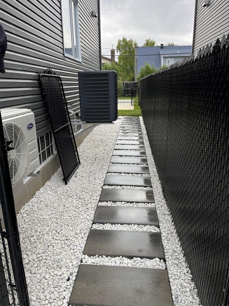 A walkway leading to a house with a black chain link fence.