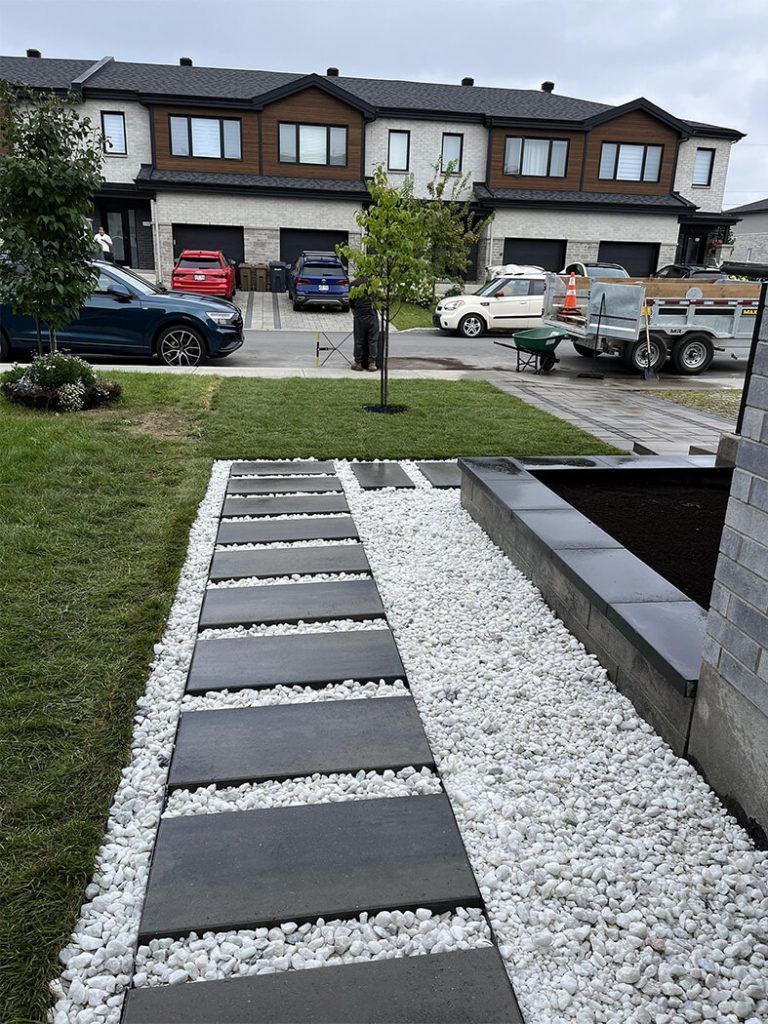 A walkway lined with black tiles and white gravel in front of a row of houses.
