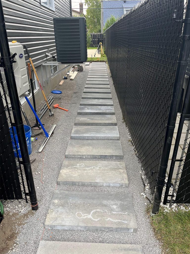A concrete walkway leading to a building next to a chain link fence.