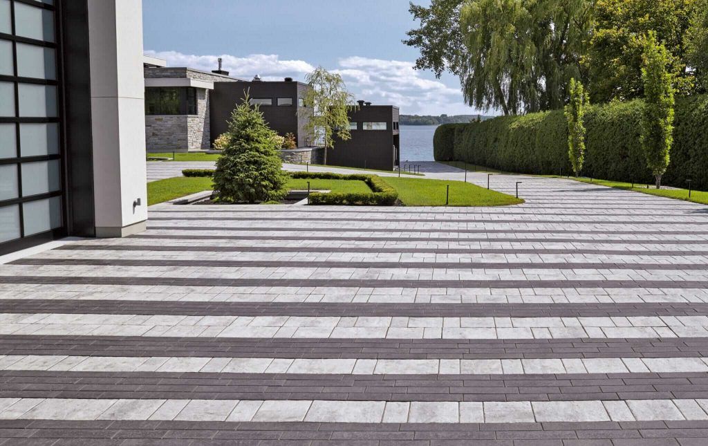 A brick driveway leading to a house with a lake in the background.