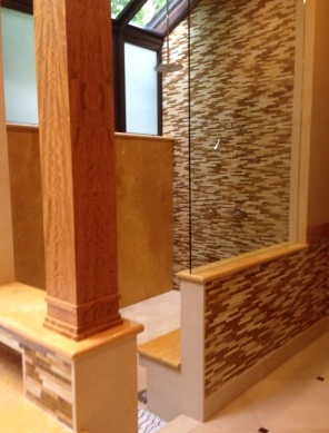 Modern bathroom with glass shower, mosaic tile wall, wooden pillar, and bench.