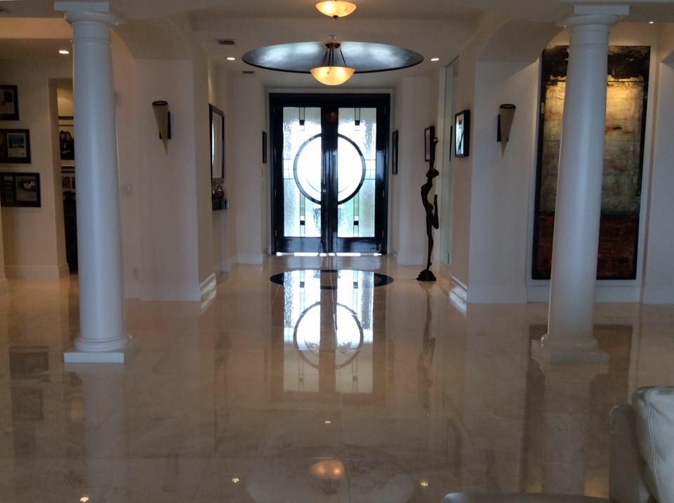 Brightly lit, polished marble hallway with ornate columns and a black double door.