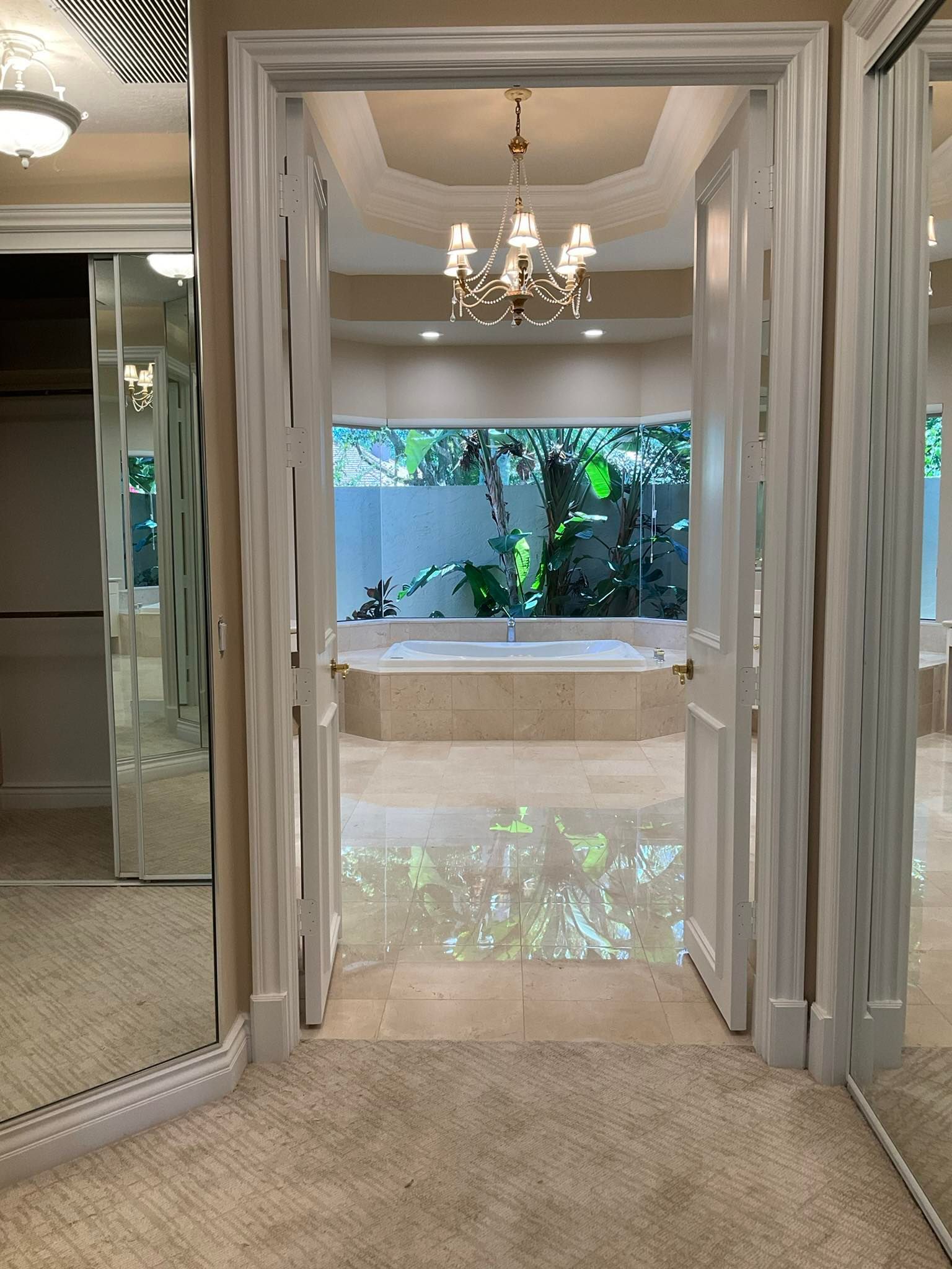 View of a bathroom through double doors, with a bathtub in the back and mirrors on the left.