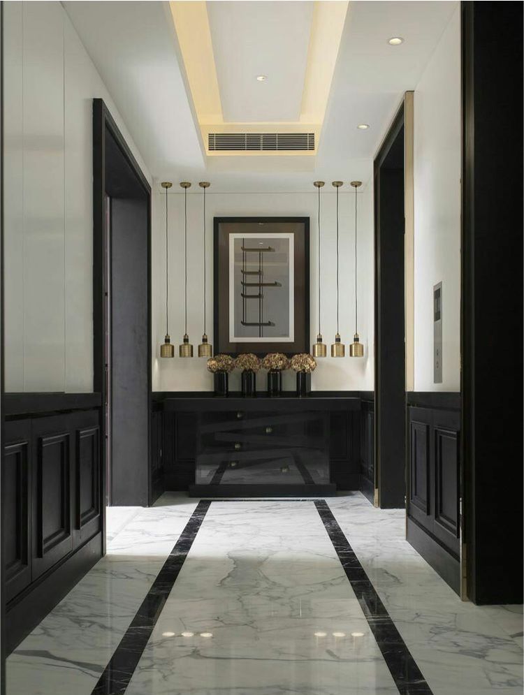 Hallway with marble floors, black trim, and a console table with artwork and hanging lights.