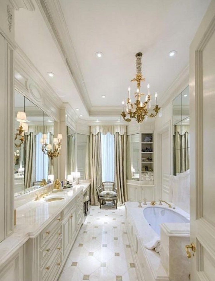 Luxurious white bathroom with marble flooring, gold chandelier, and ornate cabinetry.