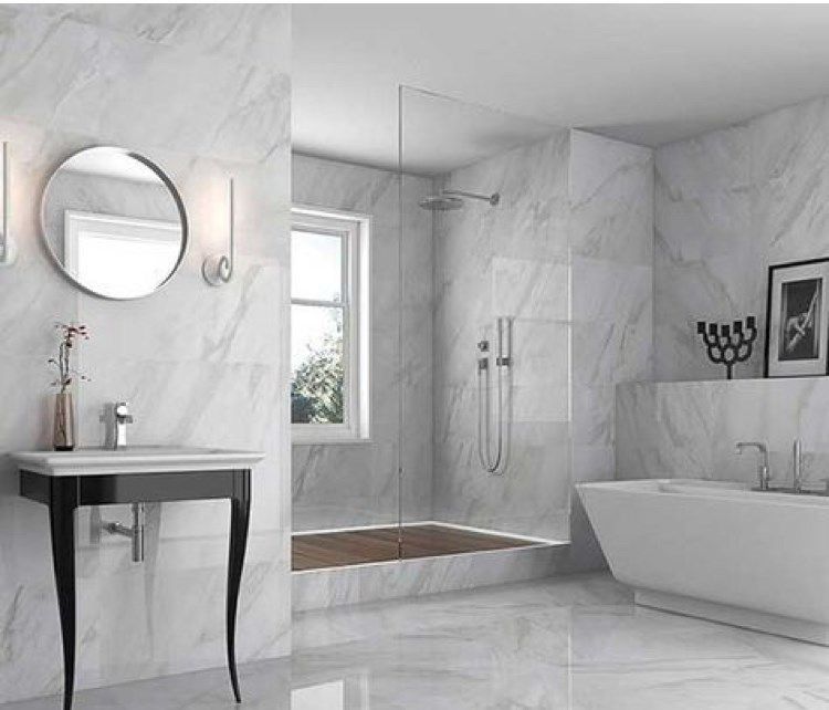 White marble-tiled bathroom with a vanity, shower, soaking tub, and window.