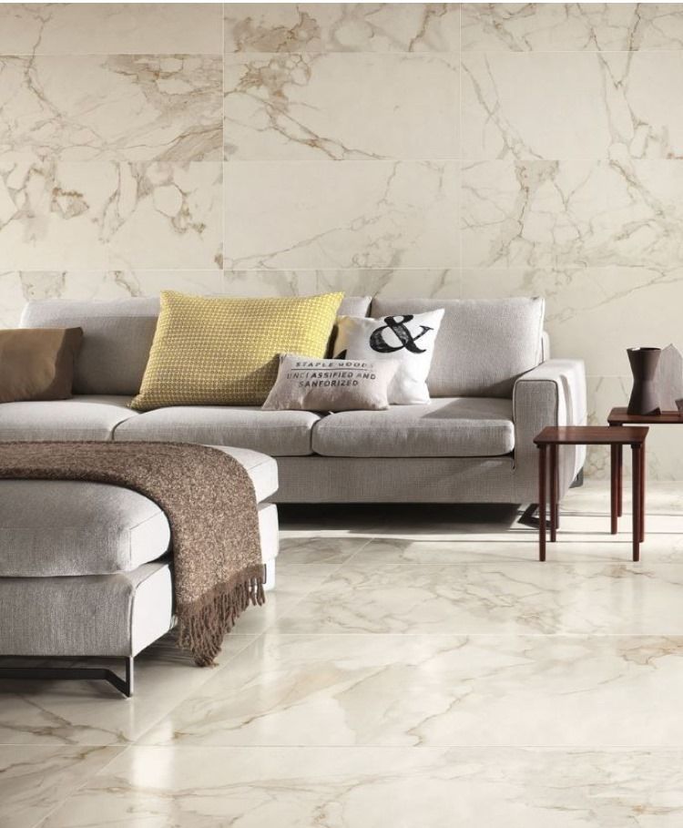 Living room with marble tile floors and walls, light gray couch with pillows, and side tables.