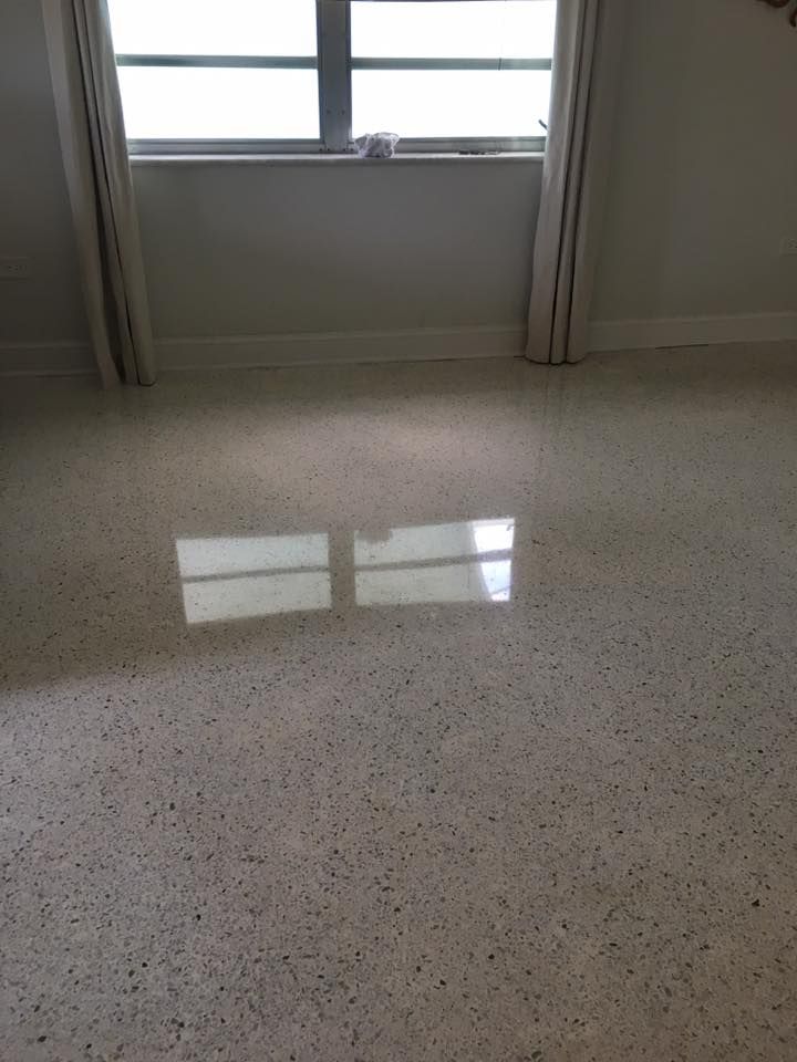 Polished terrazzo floor reflecting light from a window with curtains; neutral-toned room.