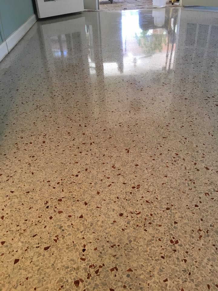 Polished concrete floor with reddish-brown aggregate, reflecting bright light.