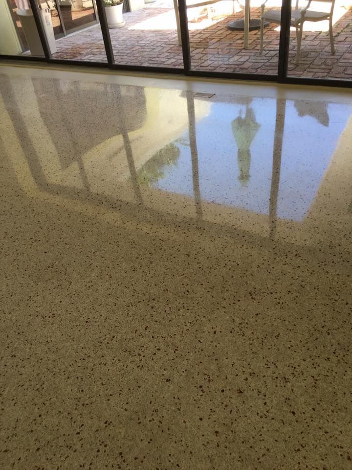 Shiny, speckled, beige flooring reflecting outdoor patio through glass doors.