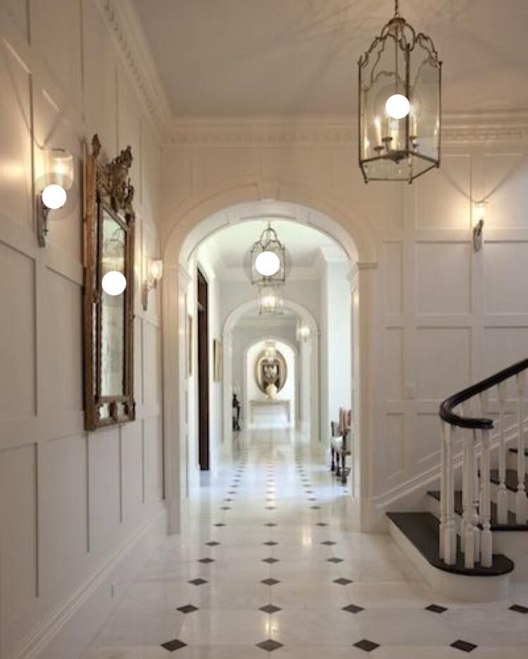 Elegant hallway with marble floors, paneled white walls, and ornate lighting.
