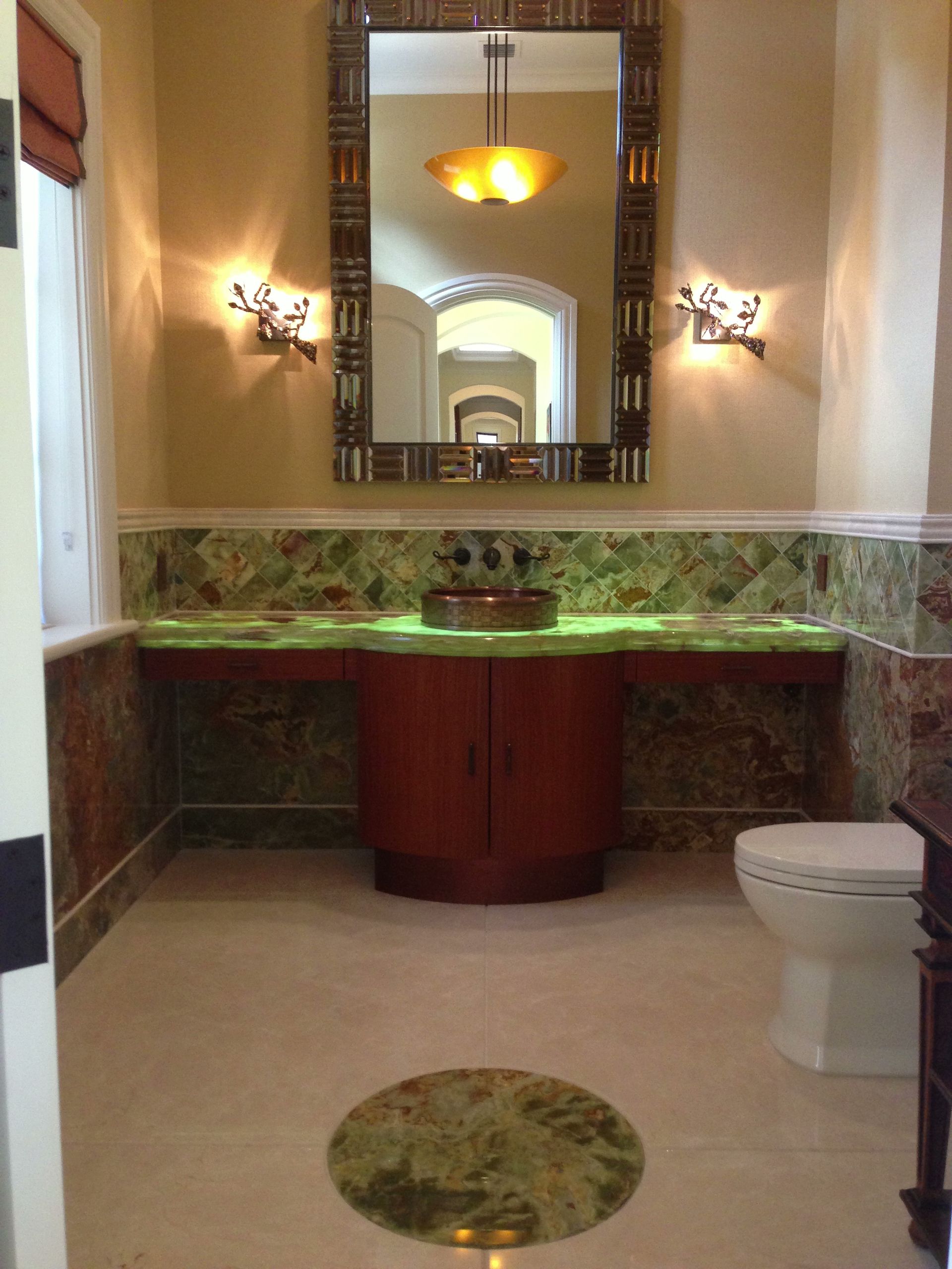 Bathroom with green countertop, ornate mirror, and circular floor inlay.