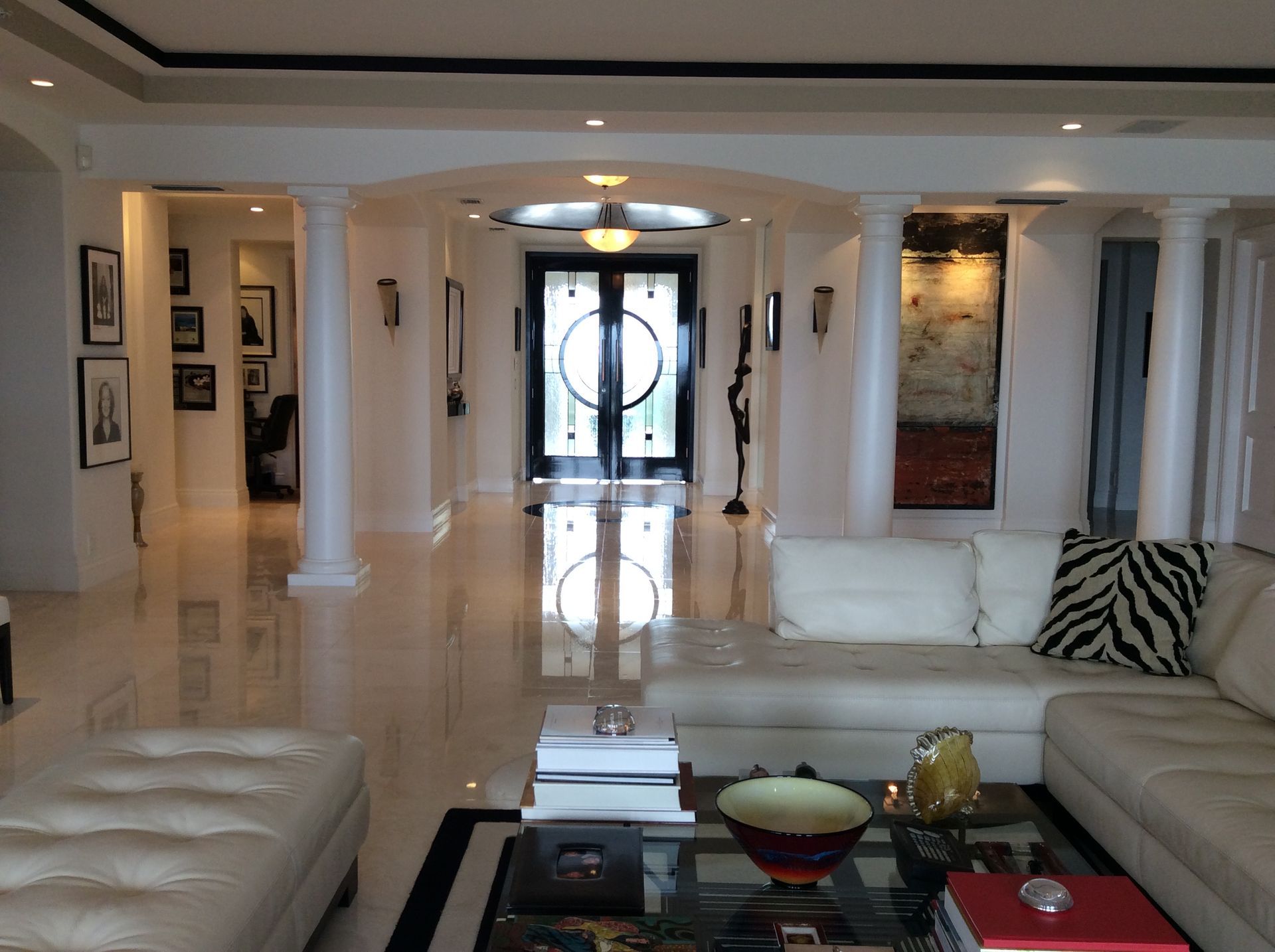 Spacious, light-filled interior with marble floors, columns, and a large black door at the end of a long hallway.