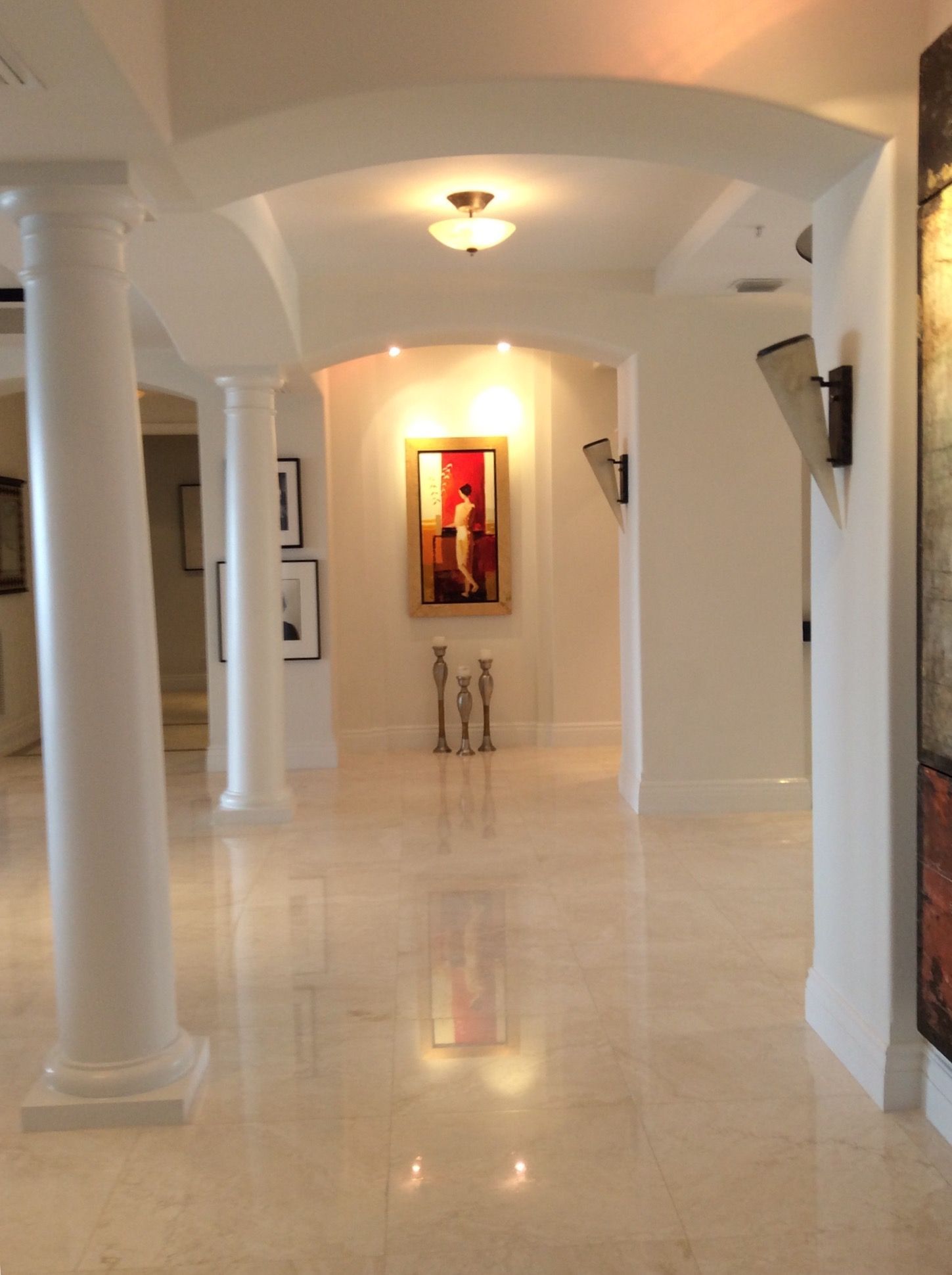 Hallway with polished marble floors, arched doorways, white pillars, and artwork.
