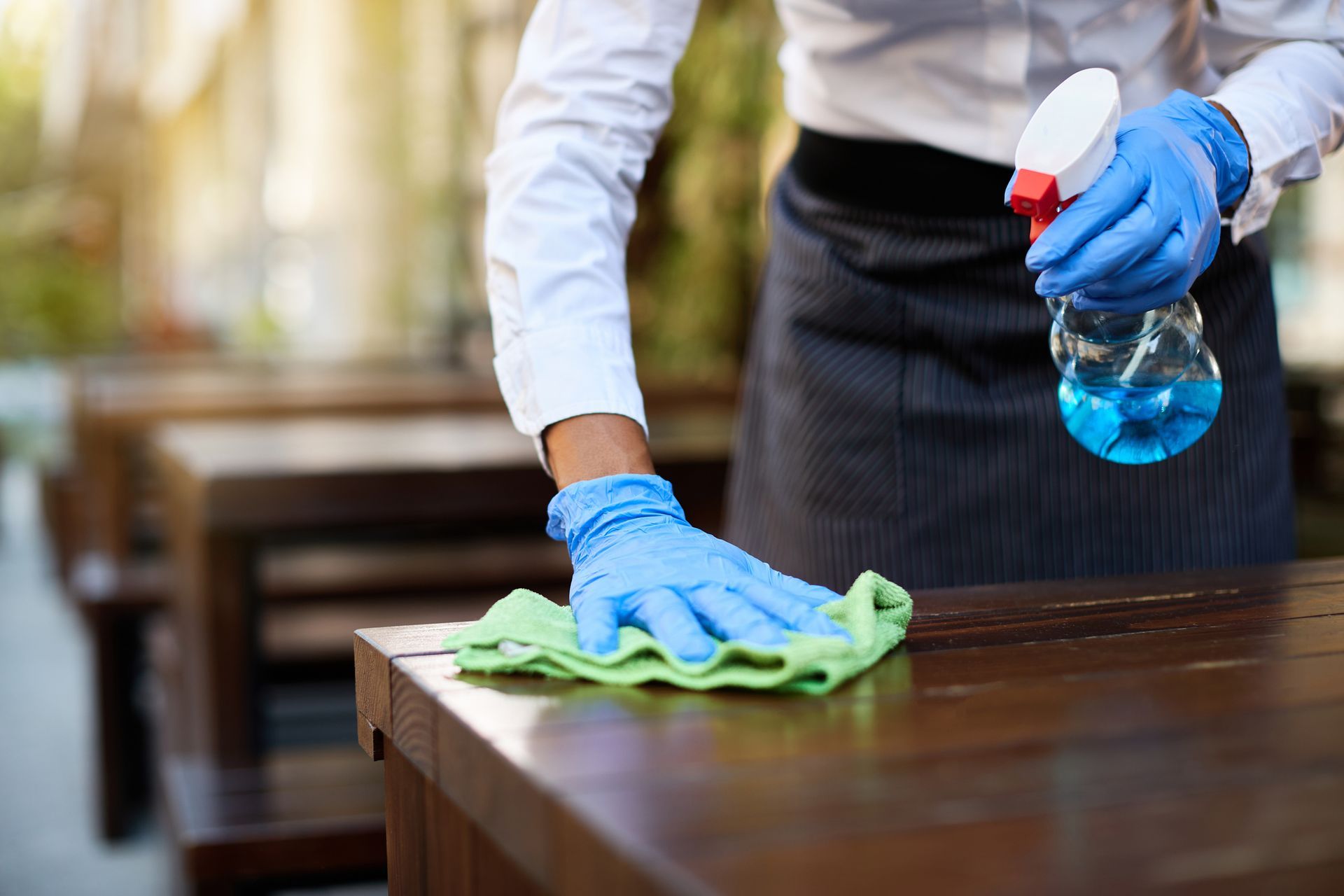 A person wearing blue gloves is cleaning a wooden table with a cloth.