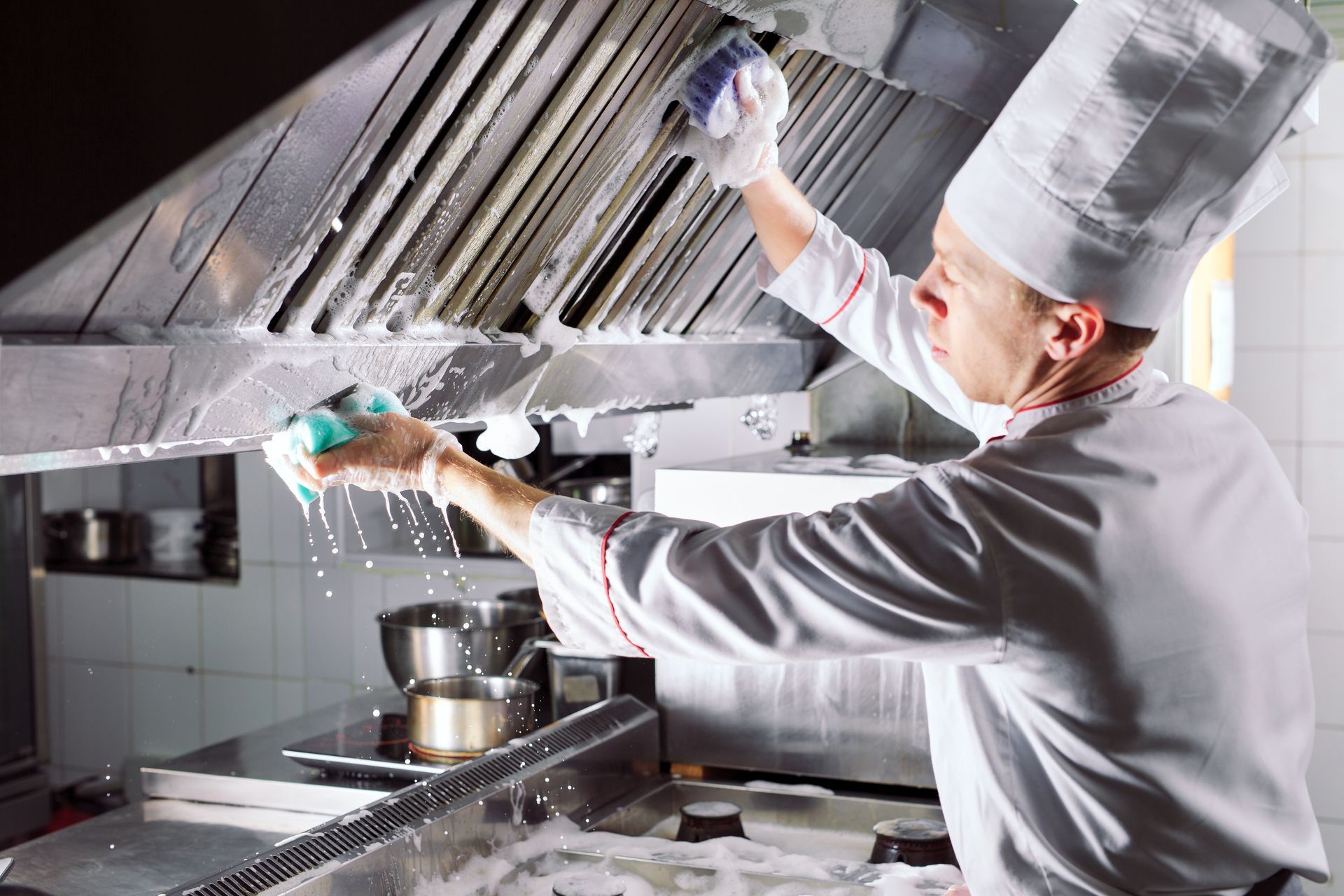 Chef cleaning a commercial kitchen vent hood with sponge.