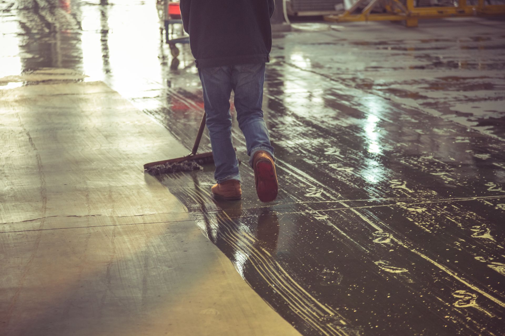 Person mopping a wet, concrete floor in a warehouse setting.