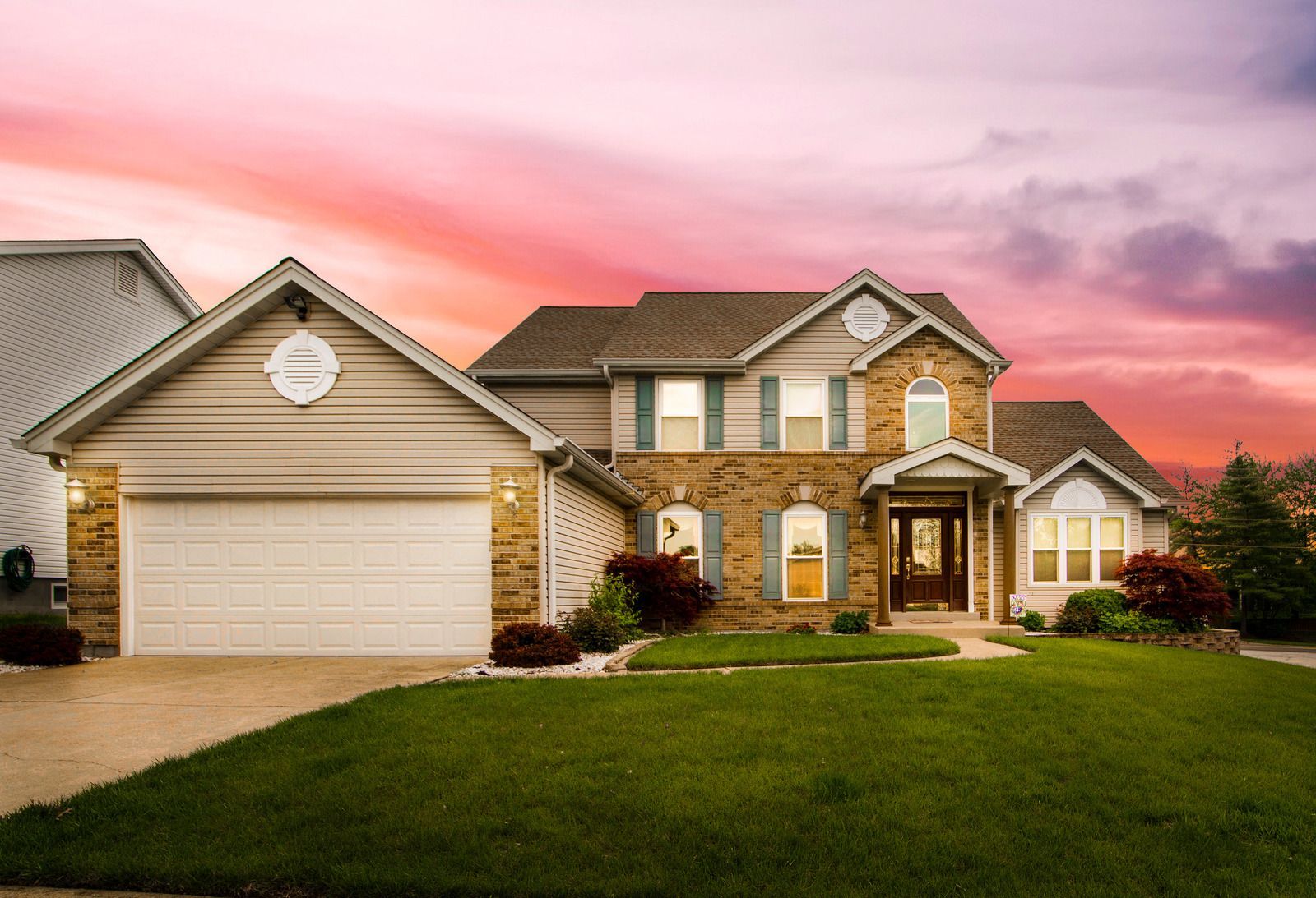 A large house with a lush green lawn and a sunset in the background.