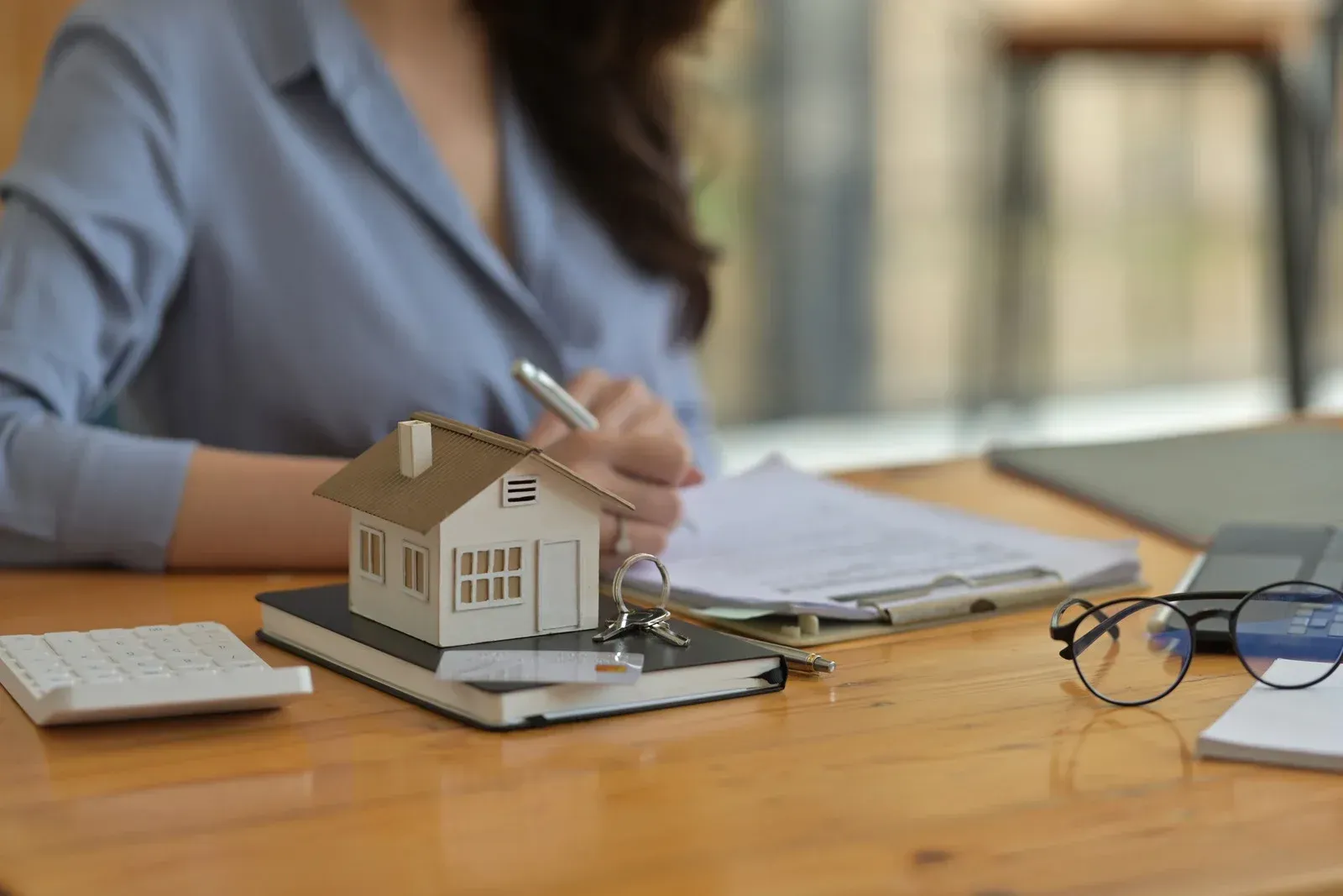 A woman is sitting at a table with a model house and a pen.