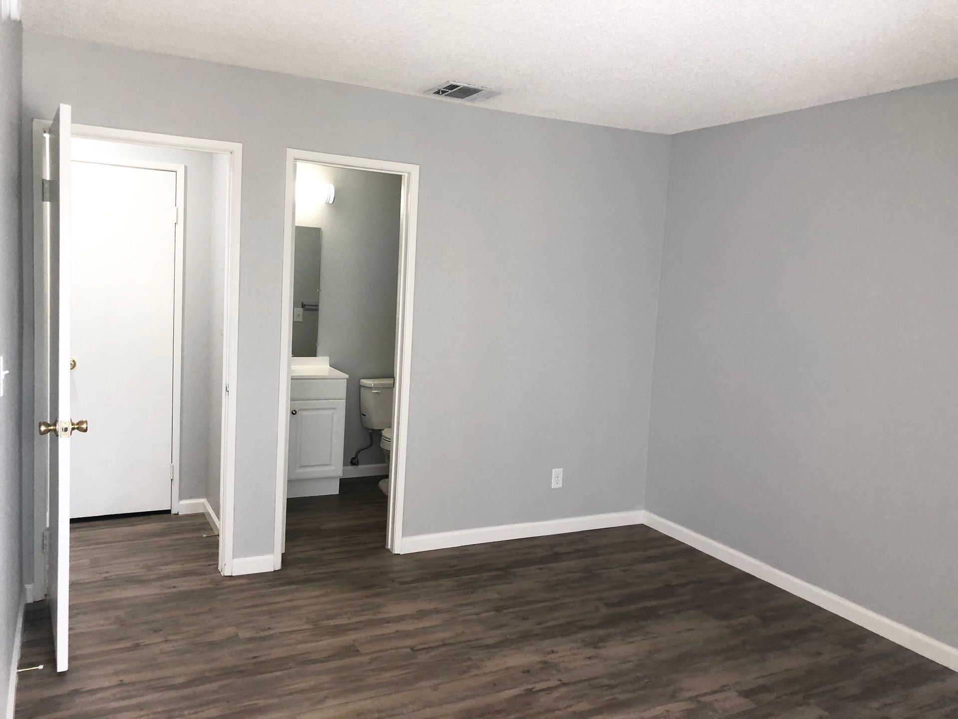 An empty room with hardwood floors and gray walls.