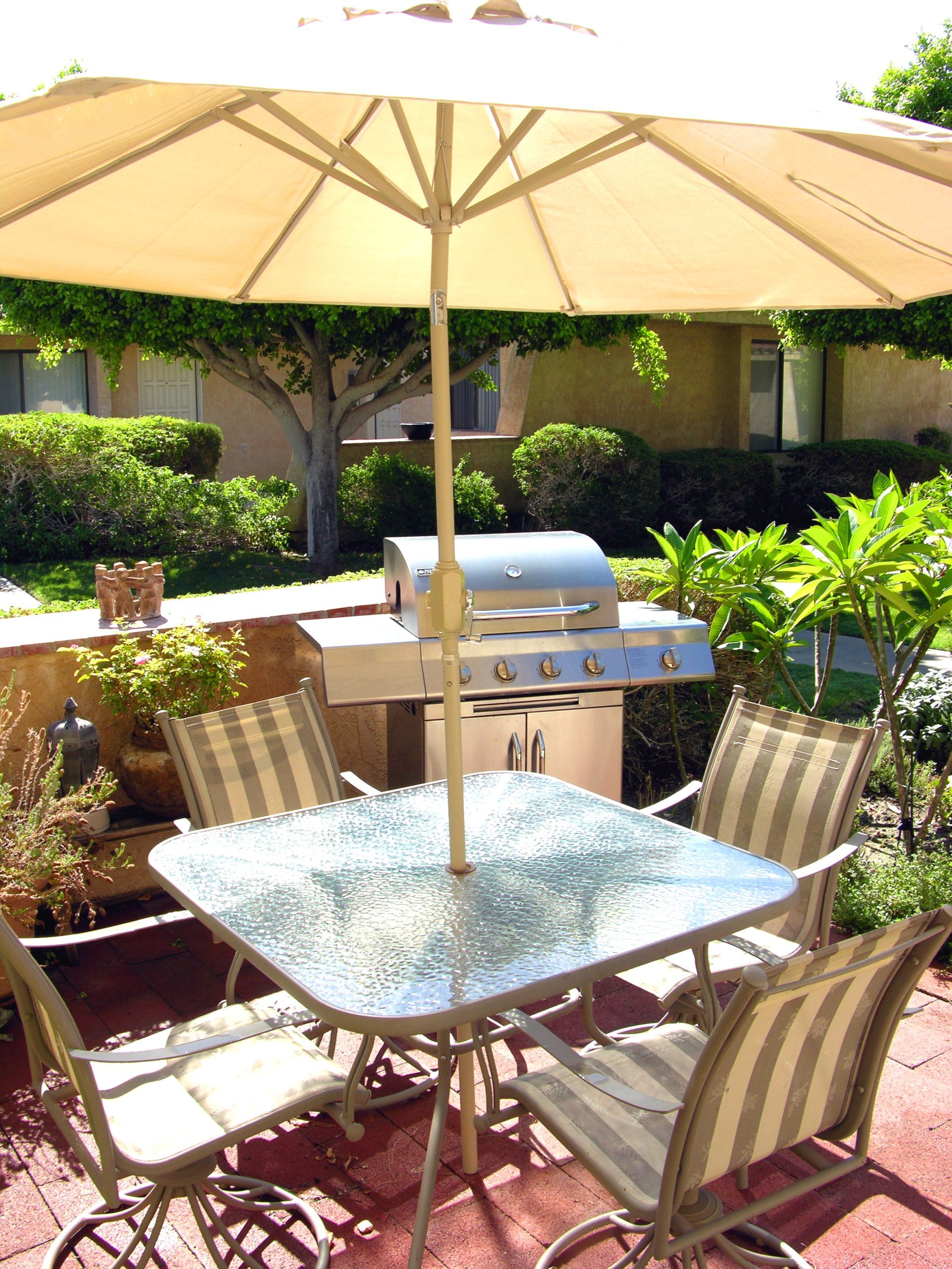A table and chairs under an umbrella with a grill in the background
