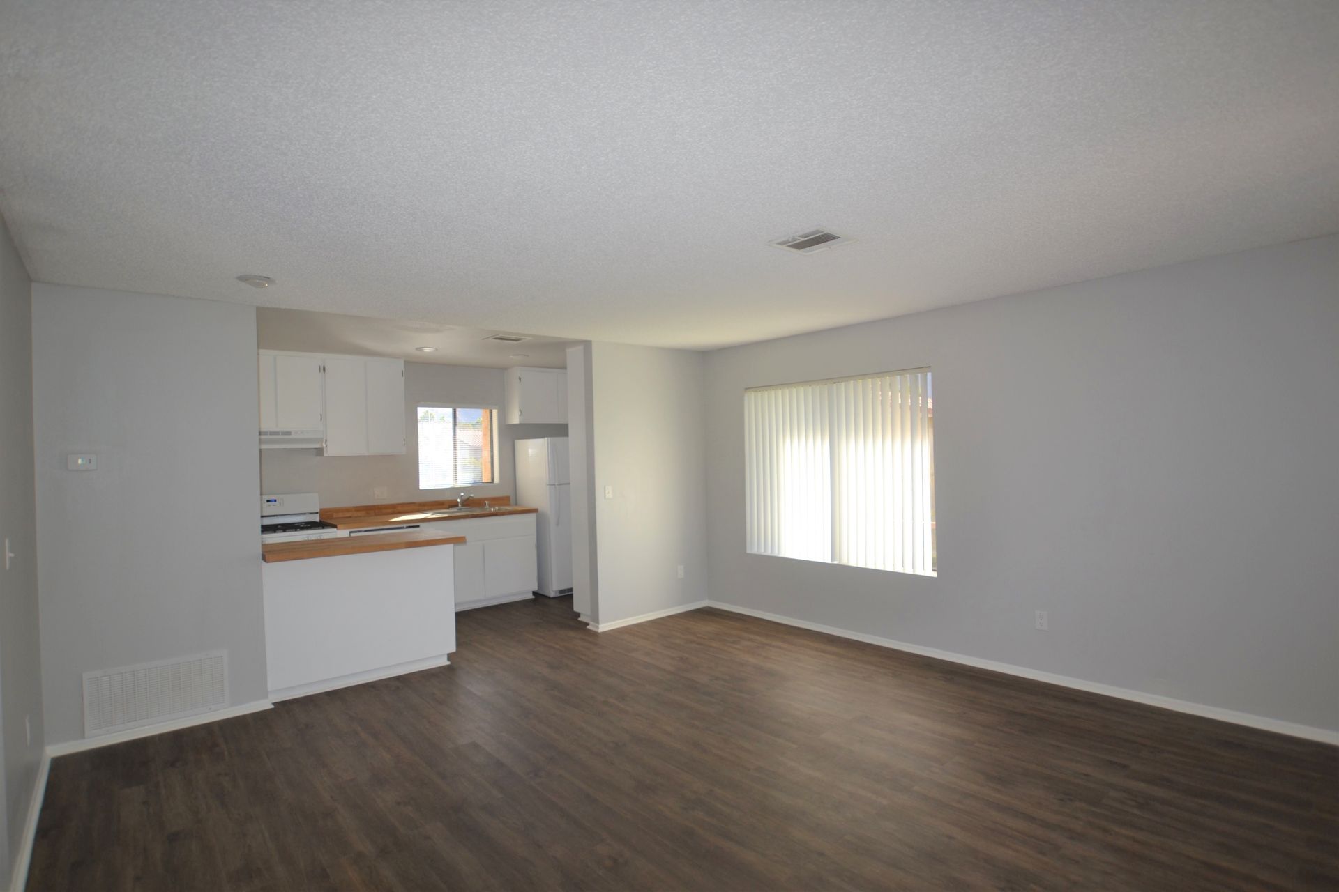 An empty living room with a kitchen in the background