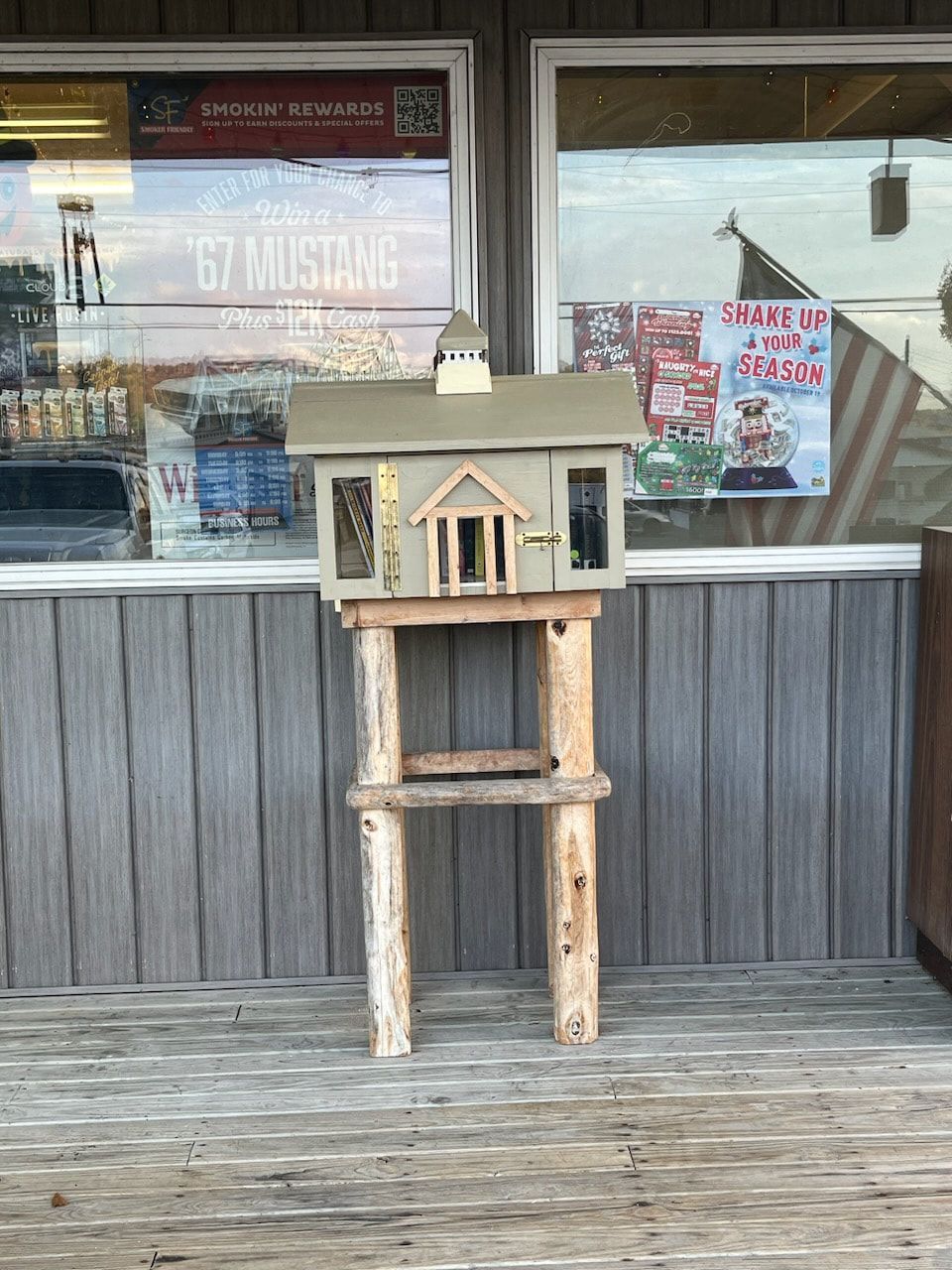 a miniature green house sits upon wooden supports in front of a building