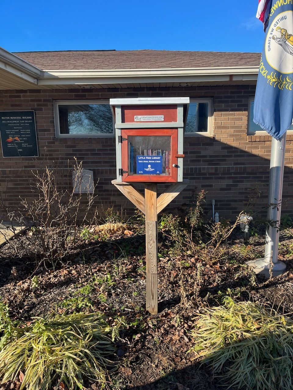 A small red box on a wooden post in front of a brick building