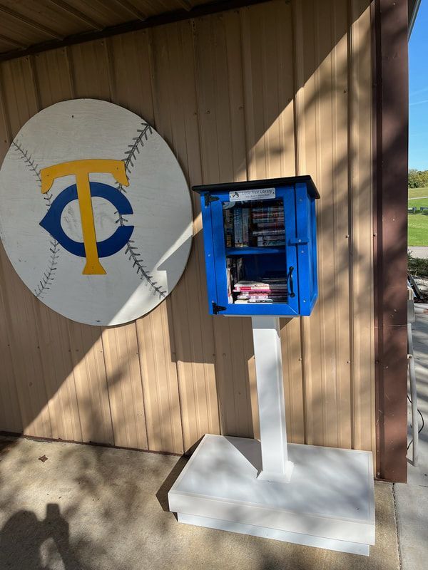 A little free library with a baseball on the wall behind it