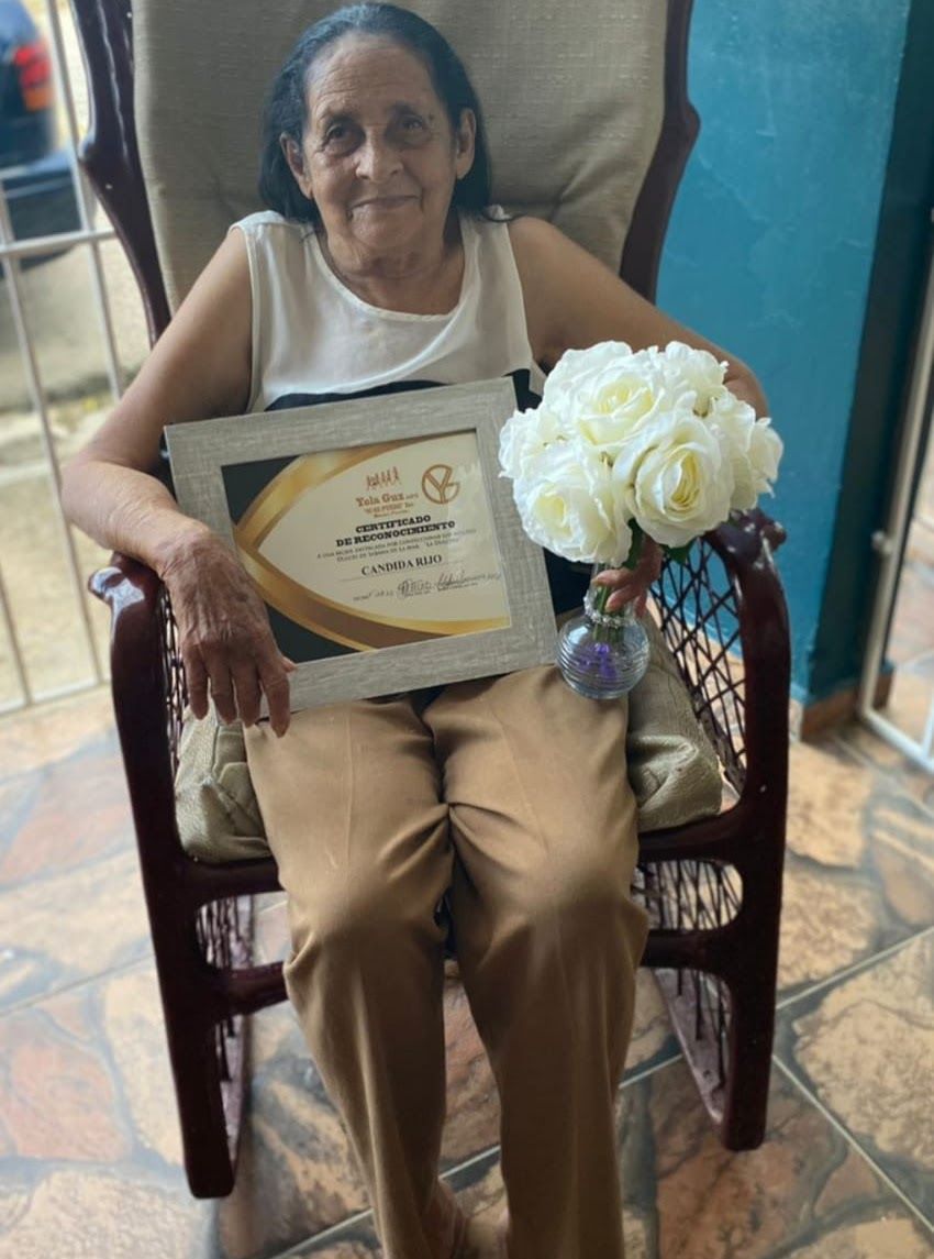 A woman is sitting in a chair holding a certificate and flowers