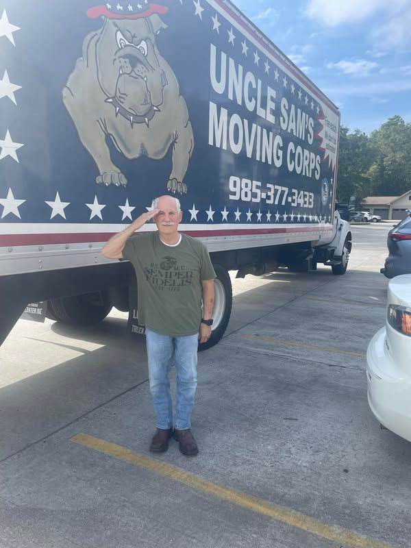 A man salutes in front of a truck that says uncle sam 's moving corps