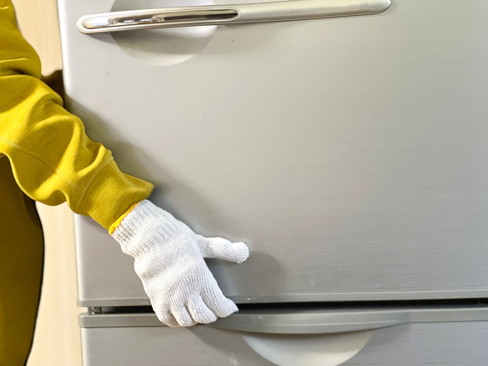 A person wearing a white glove is standing next to a refrigerator