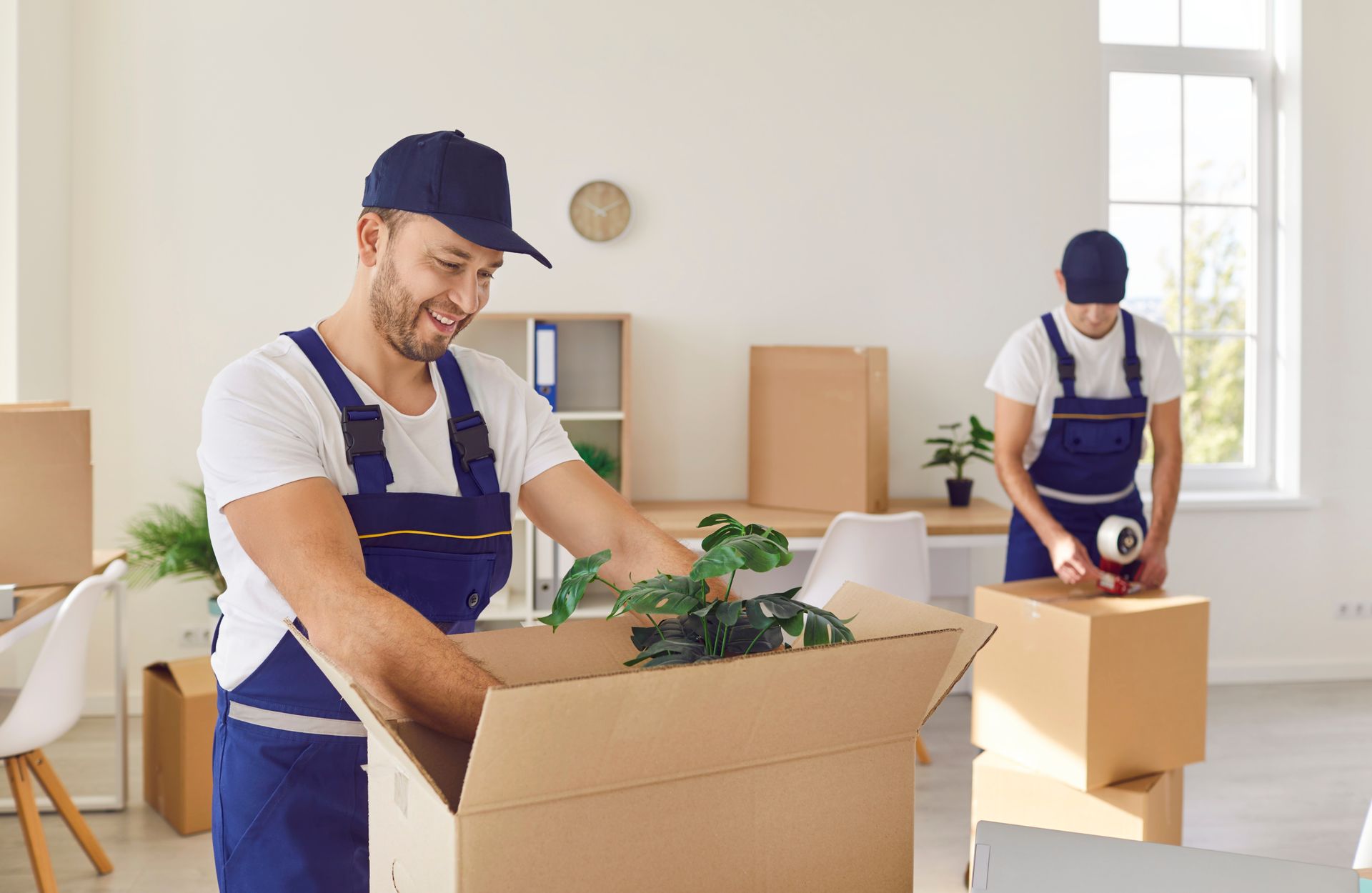Two men are packing boxes in a living room.