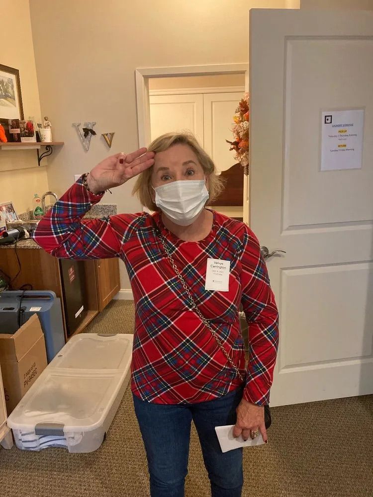 A woman wearing a face mask is saluting in a room.