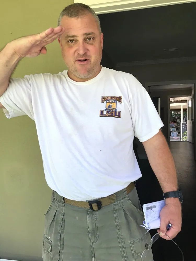 A man wearing a white shirt with the letter i on it salutes