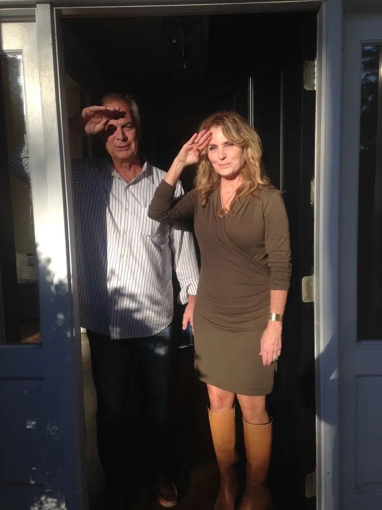 A man and a woman are standing in a doorway saluting