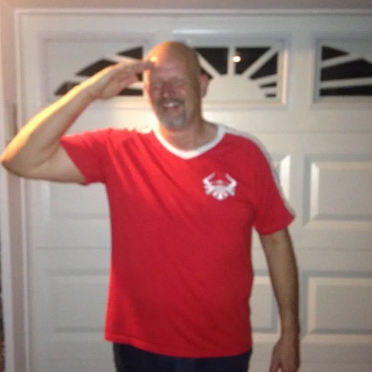A man in a red shirt salutes in front of a garage door