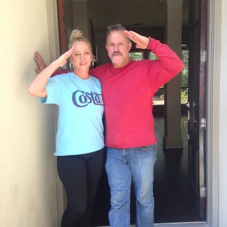 A man in a red sweater and a woman in a blue costa shirt salute