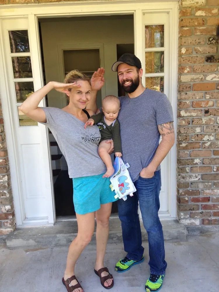 A man and woman holding a baby in front of a brick building